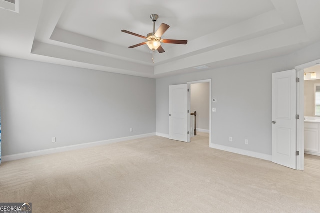 unfurnished bedroom with a tray ceiling, visible vents, light carpet, and baseboards