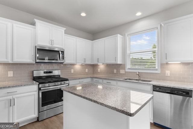 kitchen featuring a center island, white cabinetry, tasteful backsplash, a sink, and appliances with stainless steel finishes