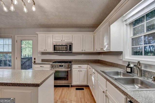 kitchen with a sink, white cabinets, stainless steel appliances, and light wood-style flooring
