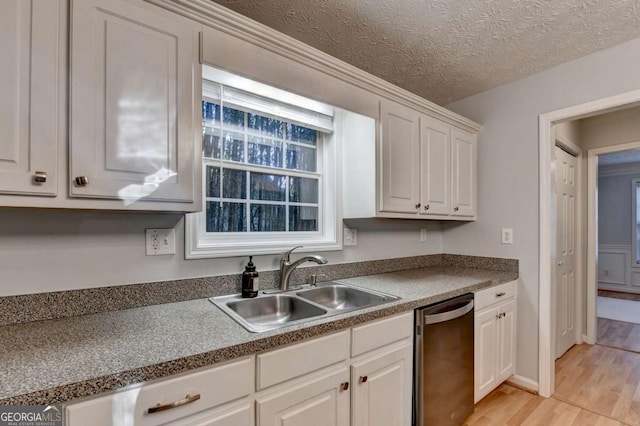 kitchen featuring dark countertops, a sink, light wood-style floors, white cabinetry, and stainless steel dishwasher