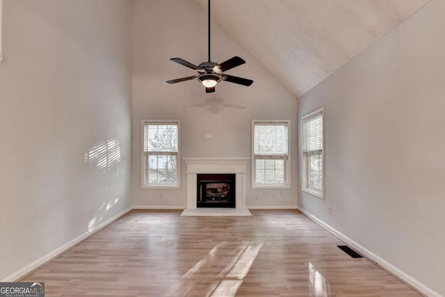 unfurnished living room with wood finished floors, baseboards, high vaulted ceiling, a fireplace with raised hearth, and a ceiling fan