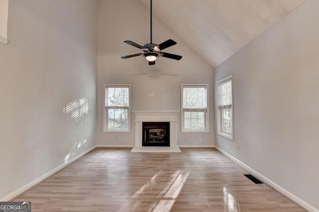 unfurnished living room with ceiling fan, a fireplace with raised hearth, high vaulted ceiling, baseboards, and wood finished floors