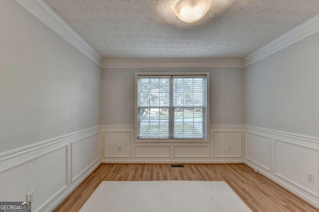 spare room with light wood-type flooring, a textured ceiling, wainscoting, and visible vents