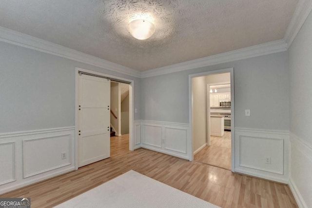 unfurnished bedroom featuring crown molding, a decorative wall, wood finished floors, a textured ceiling, and a wainscoted wall