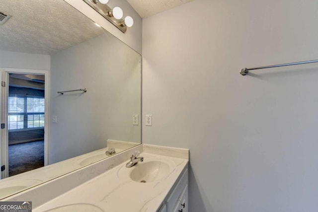 bathroom featuring double vanity, a textured ceiling, visible vents, and a sink
