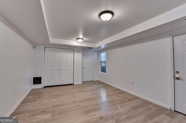 unfurnished bedroom with baseboards, a tray ceiling, and light wood-style floors