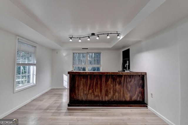 bar with baseboards, track lighting, indoor bar, a tray ceiling, and light wood-style flooring