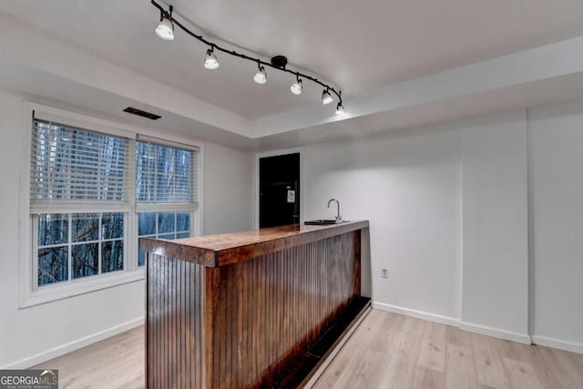 bar featuring track lighting, indoor wet bar, baseboards, light wood-style floors, and a sink