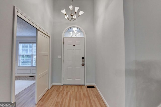 foyer entrance with baseboards, an inviting chandelier, plenty of natural light, and light wood-style flooring