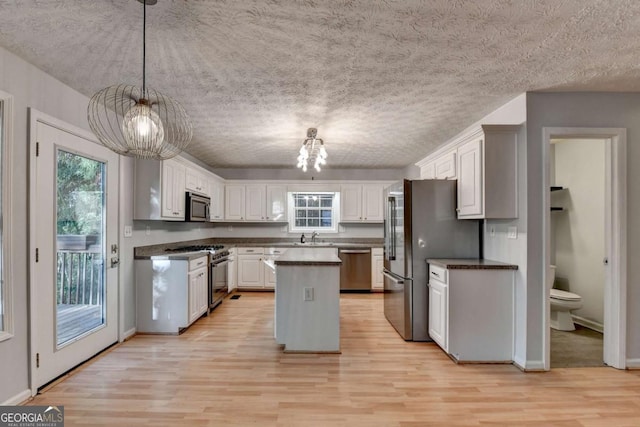 kitchen with an inviting chandelier, light wood-style floors, a center island, a sink, and appliances with stainless steel finishes