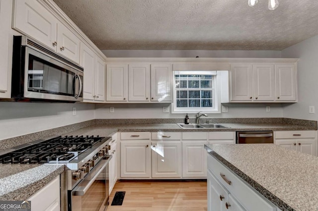 kitchen with a sink, stainless steel appliances, light wood-style flooring, and white cabinetry