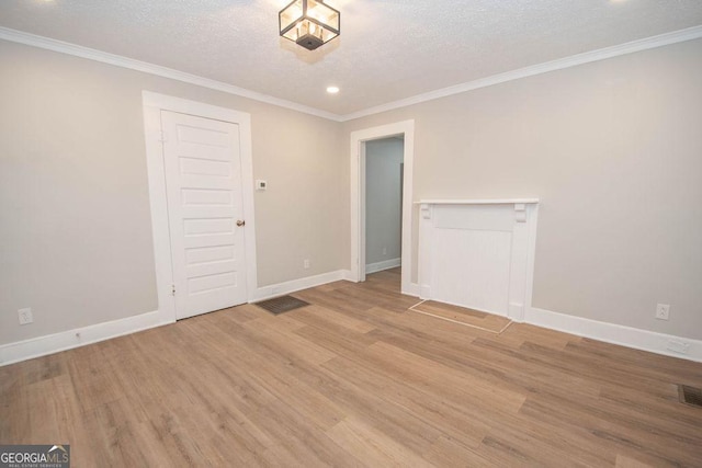 empty room featuring a textured ceiling, ornamental molding, baseboards, and light wood-style floors