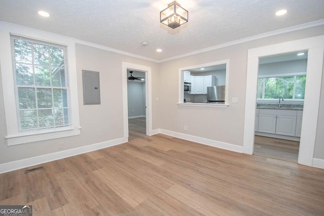 unfurnished living room with a textured ceiling, light wood-type flooring, baseboards, and electric panel