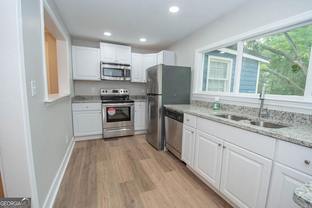 kitchen featuring a sink, light stone counters, light wood-style floors, stainless steel appliances, and white cabinetry