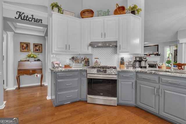 kitchen featuring decorative backsplash, gray cabinets, under cabinet range hood, stainless steel range with gas stovetop, and a sink