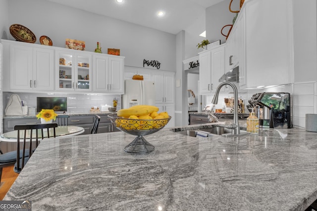 kitchen featuring stone counters, a high ceiling, white refrigerator with ice dispenser, and white cabinets