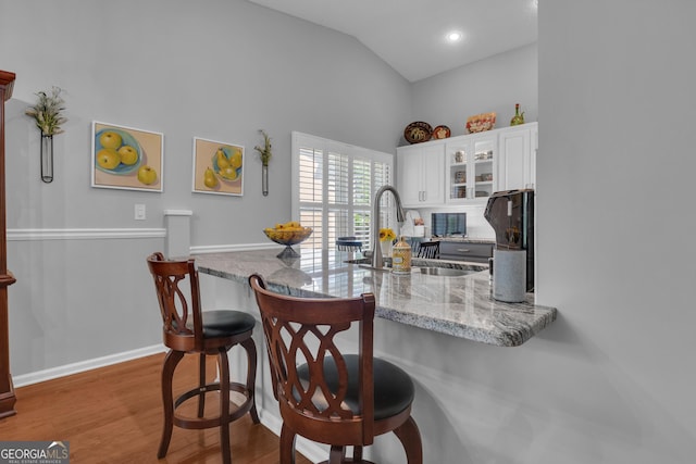 kitchen with a kitchen bar, light stone countertops, a sink, white cabinets, and glass insert cabinets