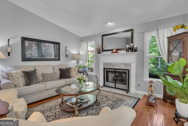 living room featuring a wealth of natural light, wood finished floors, vaulted ceiling, and a premium fireplace