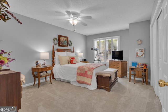bedroom with a closet, light carpet, baseboards, a textured ceiling, and a ceiling fan