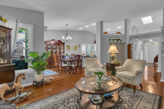 living area with a chandelier, vaulted ceiling with skylight, and hardwood / wood-style flooring