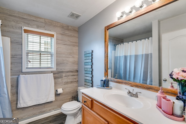 full bath with visible vents, wood walls, vanity, wood finished floors, and toilet