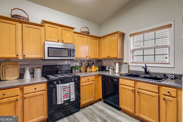 kitchen with dark countertops, tasteful backsplash, a sink, light wood finished floors, and black appliances