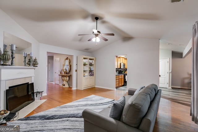 living room featuring a ceiling fan, a fireplace with flush hearth, wood finished floors, baseboards, and lofted ceiling