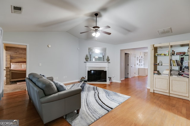 living area featuring visible vents, a ceiling fan, a glass covered fireplace, and wood finished floors