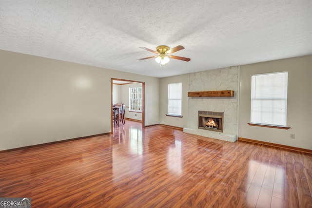 175 Laney Ct, Mcdonough, GA 30252 - unfurnished living room featuring ceiling fan, a textured ceiling, a stone fireplace, wood finished floors, and baseboards