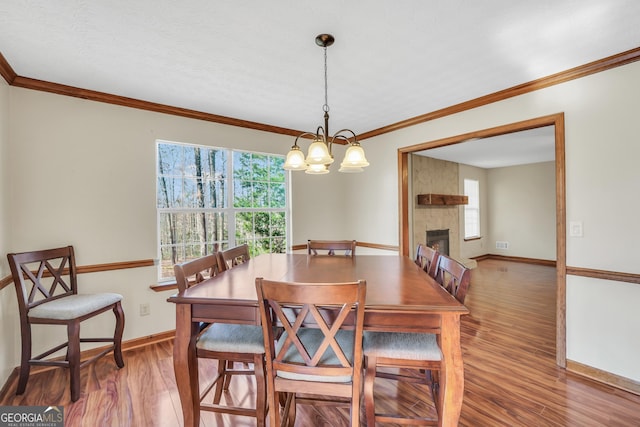 175 Laney Ct, Mcdonough, GA 30252 - dining space featuring crown molding, a fireplace, a chandelier, baseboards, and wood finished floors
