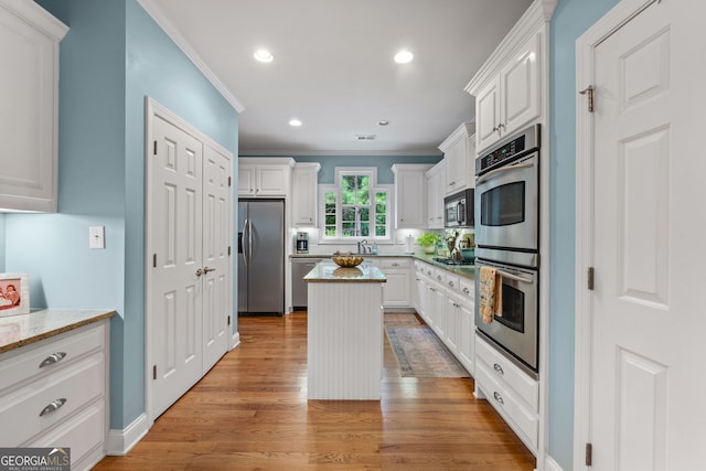 kitchen featuring ornamental molding, a kitchen island, white cabinetry, light stone counters, and appliances with stainless steel finishes