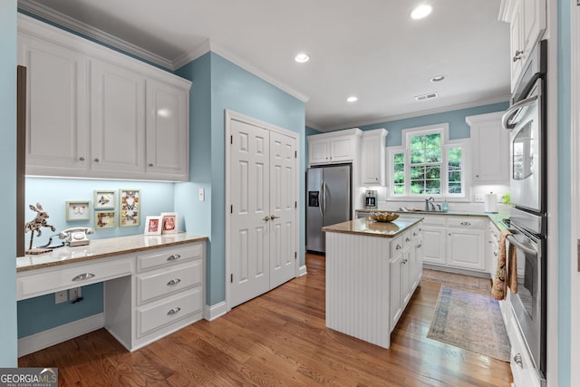 kitchen featuring crown molding, white cabinetry, stainless steel fridge, and built in desk
