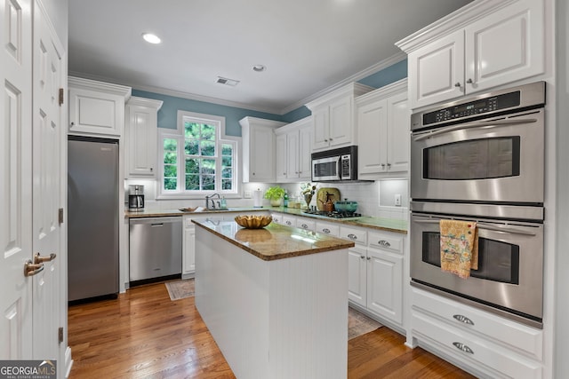 kitchen featuring a kitchen island, visible vents, ornamental molding, stainless steel appliances, and white cabinetry