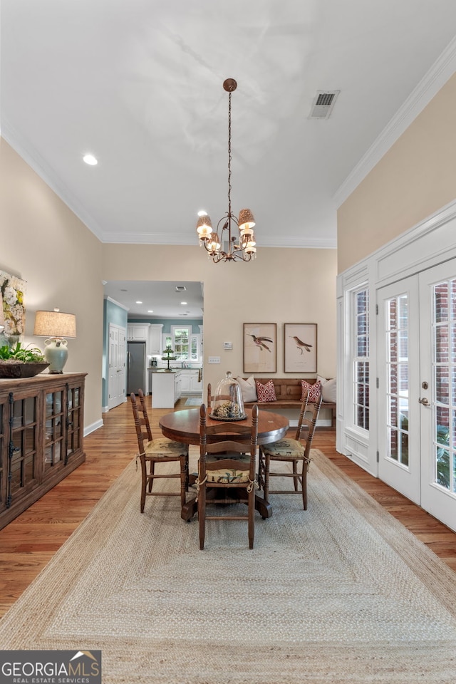 dining room featuring an inviting chandelier, french doors, light wood-style flooring, visible vents, and ornamental molding