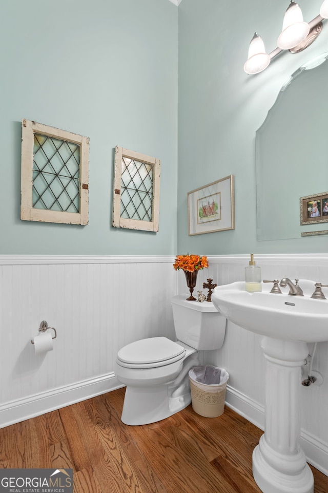 half bathroom with toilet, a sink, wood finished floors, and a wainscoted wall