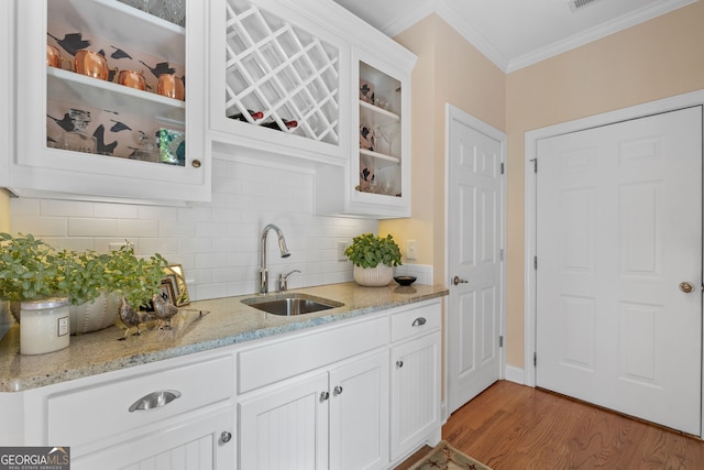 interior space with ornamental molding, light stone countertops, glass insert cabinets, tasteful backsplash, and a sink