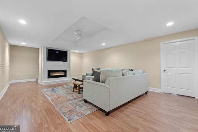 living room with baseboards, a fireplace, a ceiling fan, and light wood-type flooring