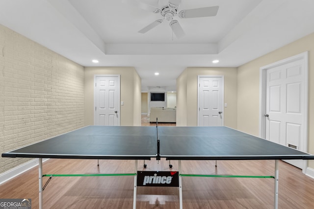 recreation room with recessed lighting, brick wall, ceiling fan, and a tray ceiling