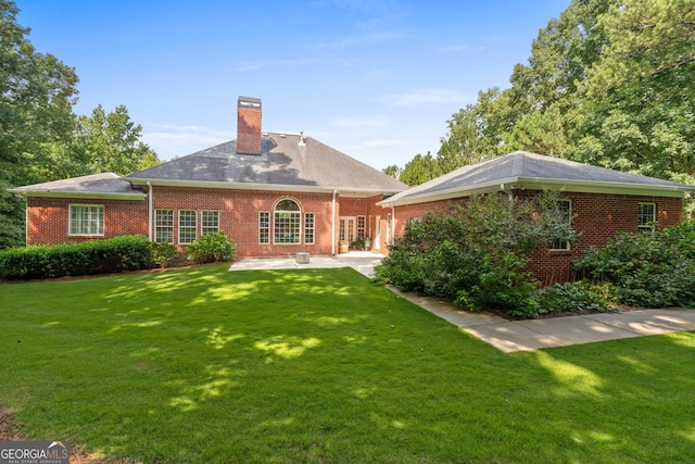 back of house featuring brick siding, a patio area, a lawn, and a chimney