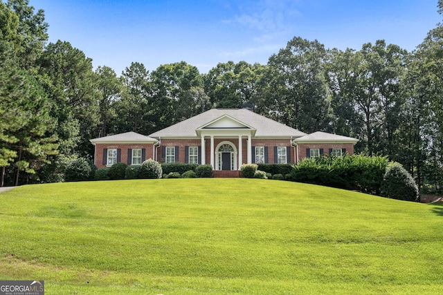greek revival inspired property with brick siding and a front yard