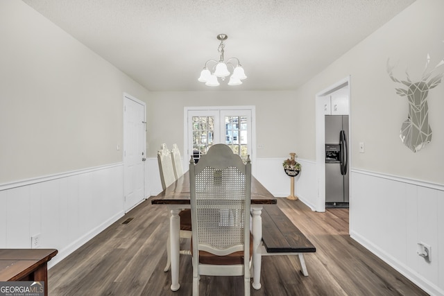 dining area with a textured ceiling, an inviting chandelier, wainscoting, and dark wood finished floors