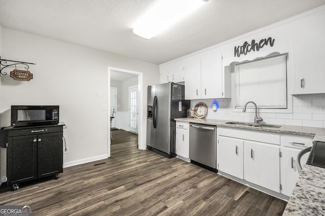 kitchen with appliances with stainless steel finishes, tasteful backsplash, dark wood finished floors, a sink, and white cabinetry