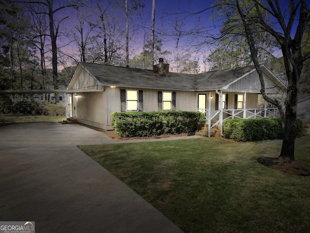 ranch-style home with stairs, a front lawn, a chimney, covered porch, and driveway