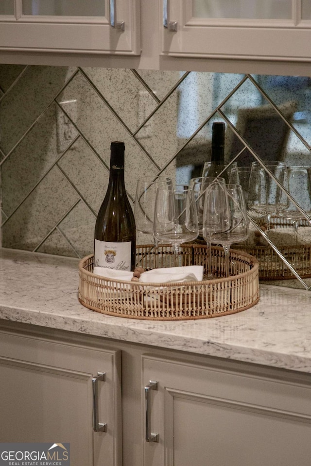 details with glass insert cabinets, decorative backsplash, light stone countertops, and white cabinets