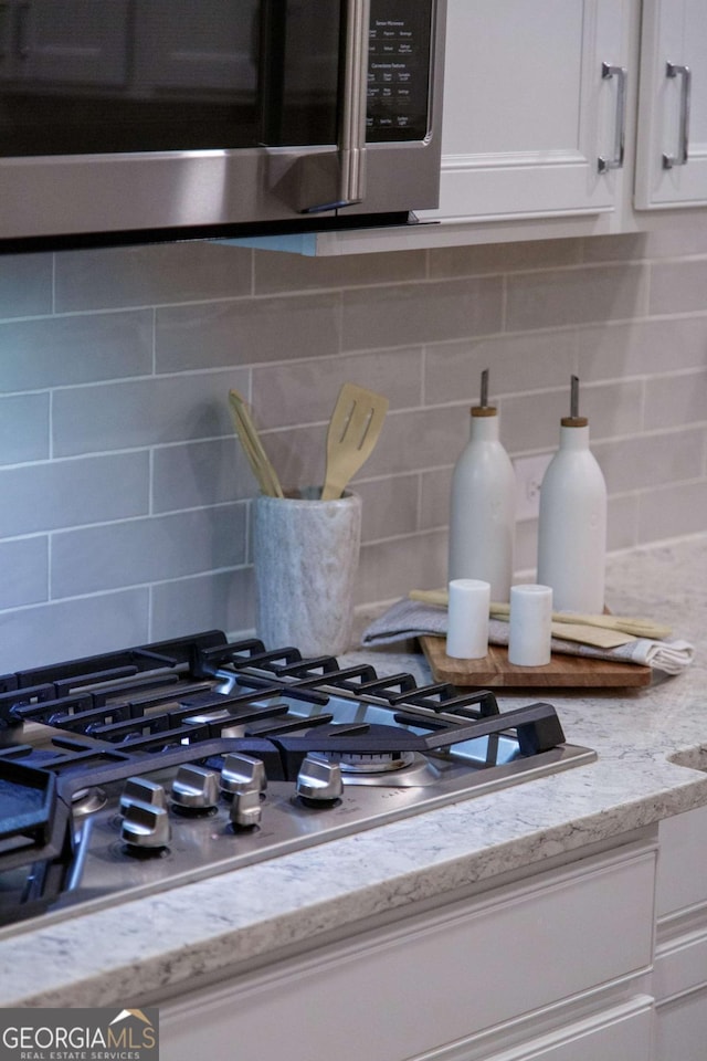 details with white cabinets, stainless steel appliances, light stone countertops, and tasteful backsplash