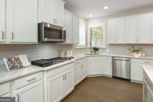 kitchen featuring decorative backsplash, dark wood-type flooring, white cabinetry, a sink, and stainless steel appliances