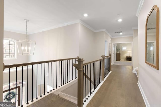 hallway featuring an inviting chandelier, ornamental molding, visible vents, wood finished floors, and an upstairs landing