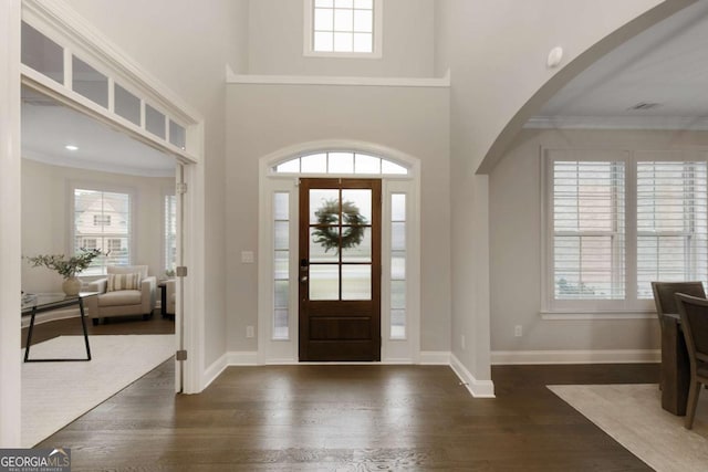 foyer entrance with crown molding, arched walkways, baseboards, and wood finished floors