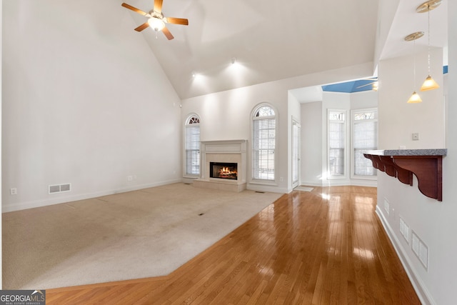 unfurnished living room with a premium fireplace, a ceiling fan, high vaulted ceiling, and visible vents