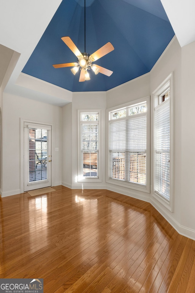 spare room with baseboards, a ceiling fan, wood finished floors, and a wealth of natural light